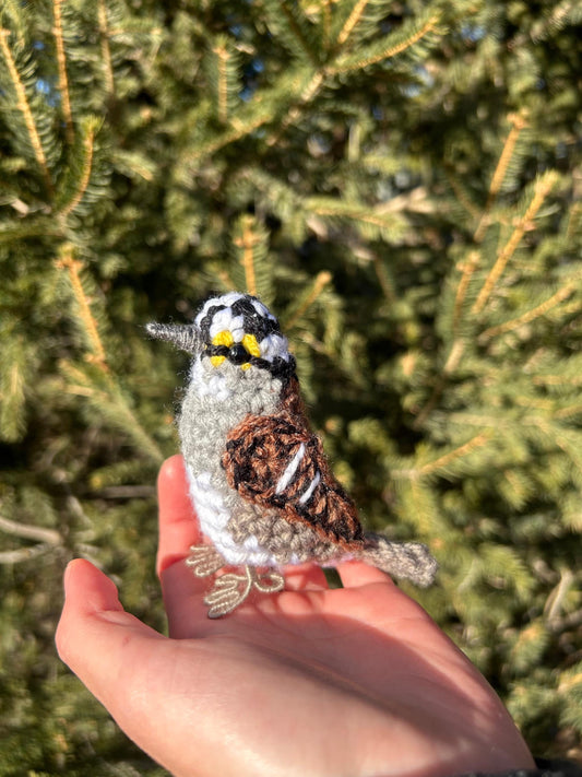 Hand holding a small bird figurine in front of a green tree