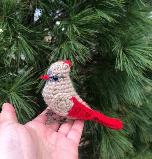 Hand holding a crocheted cardinal bird against a green leafy background