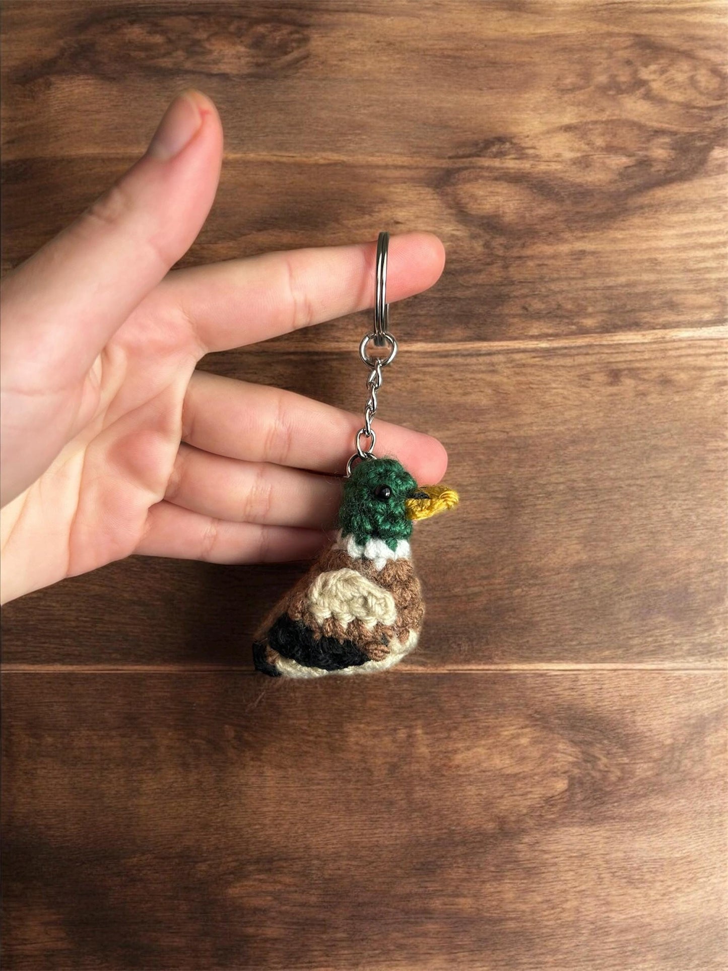 Hand holding a small crocheted keychain with a wooden background
