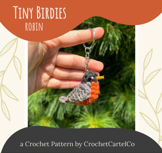 A crocheted robin keychain held by a hand with a green leafy background, featuring 'Tiny Birdies Robin Crochet Pattern' by CrochetCartelCo.