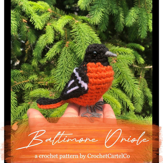 Crocheted Baltimore Oriole pattern, shown held in a hand with green foliage in the background