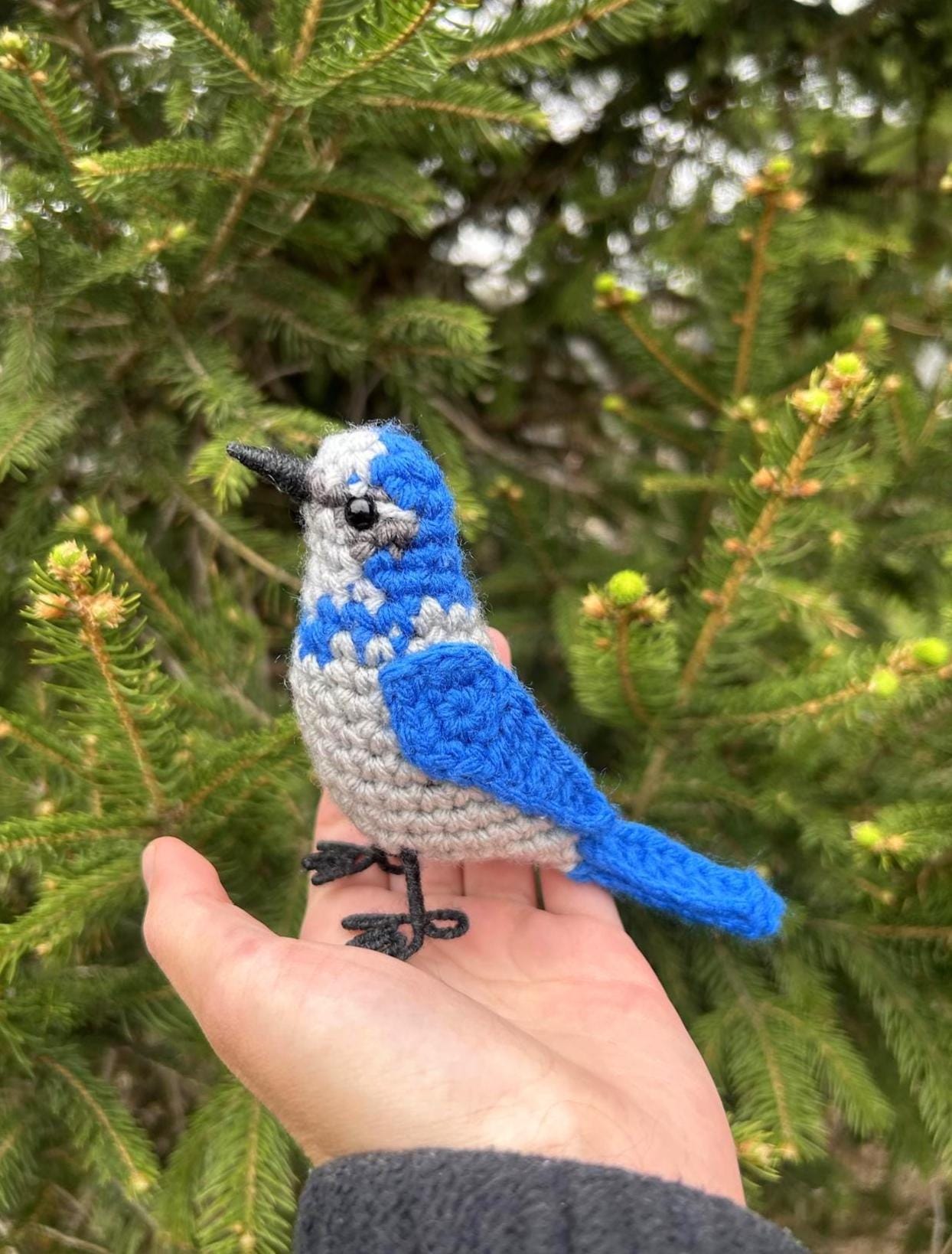 Crocheted blue bird held in a hand with a green tree background