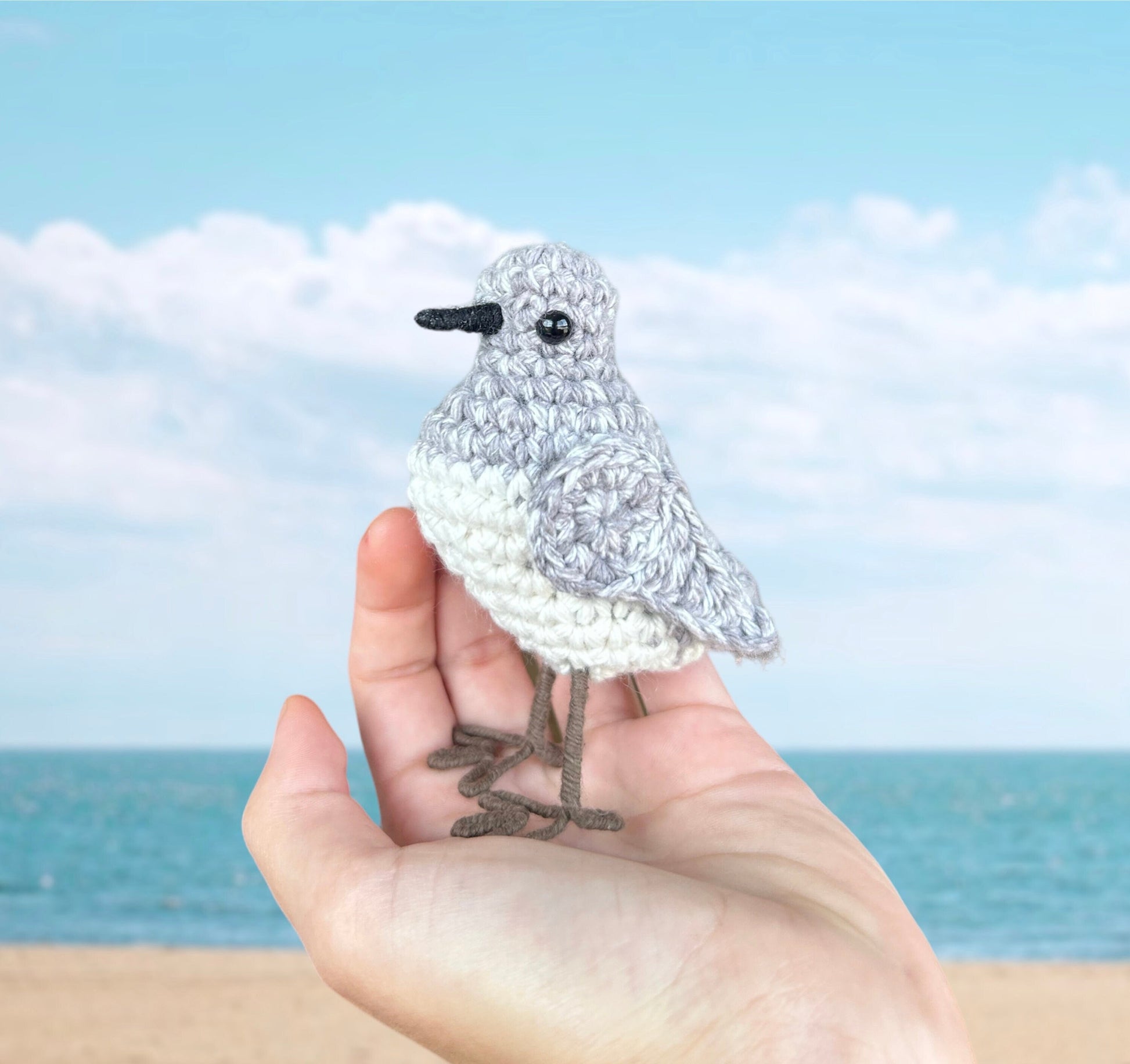 Crocheted bird held in a hand with a beach background