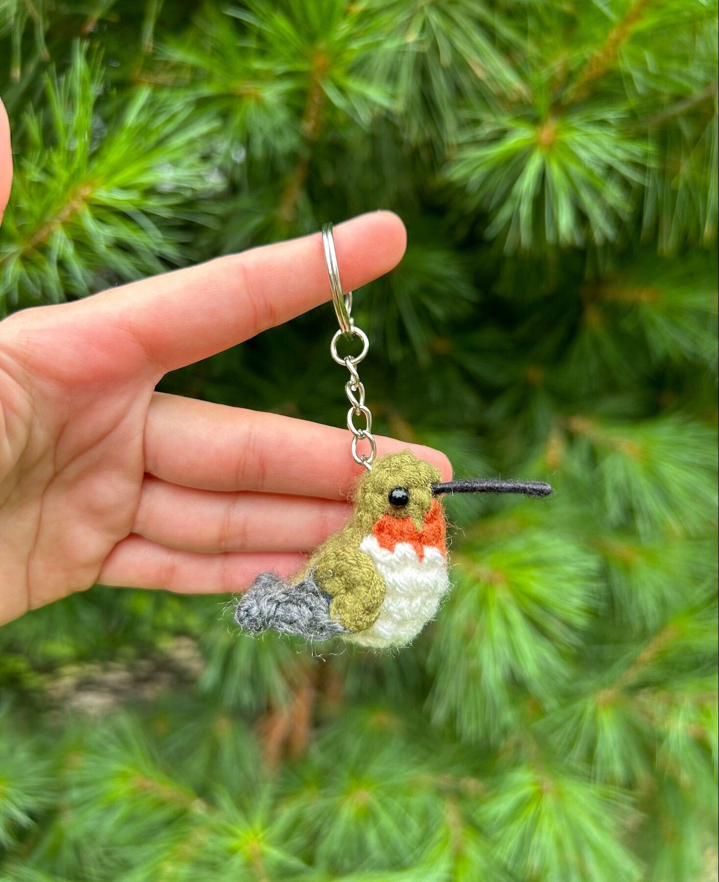 Hand holding a crocheted hummingbird keychain with a green leafy background