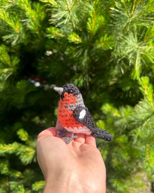 Hand holding a small crocheted bird against a green tree background
