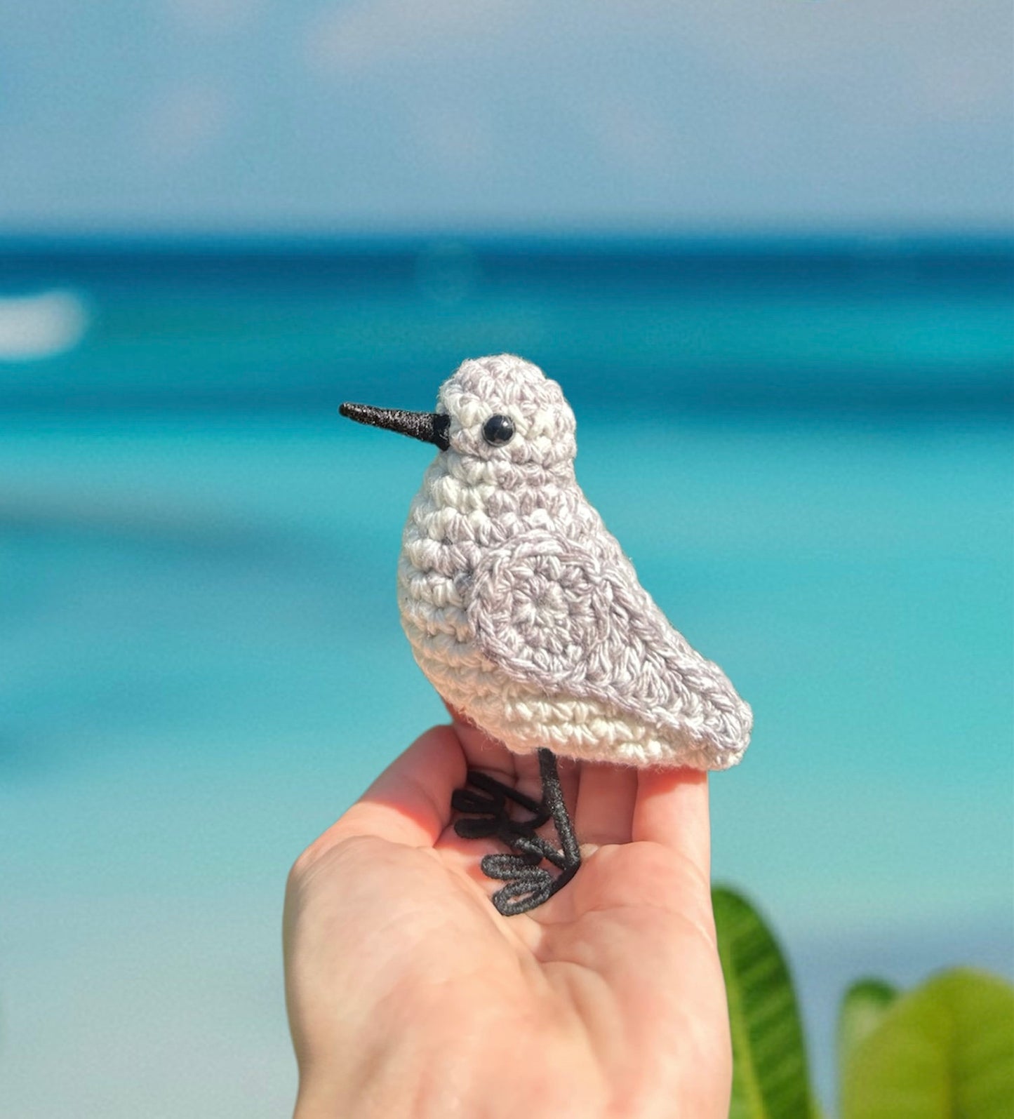 Crocheted bird held in a hand with a beach background