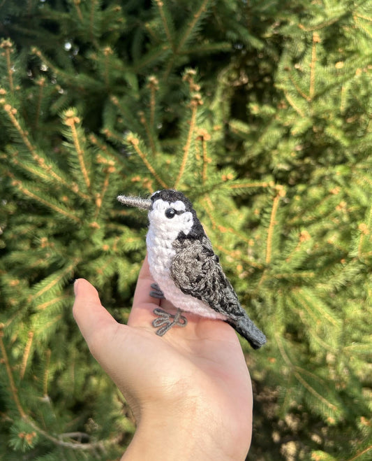 Hand holding a small bird figurine against a green tree background