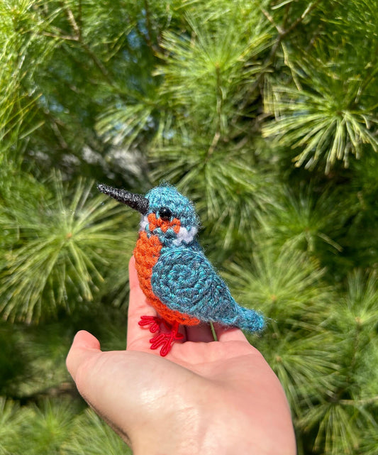 Hand holding a colorful crocheted bird against a green leafy background