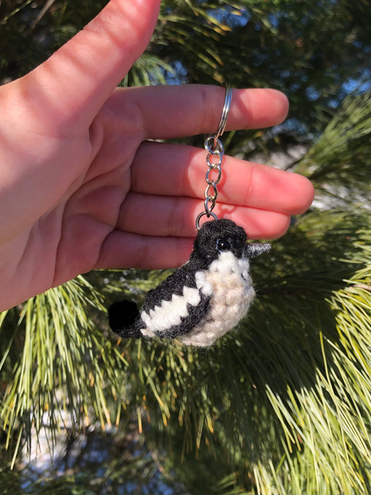 Hand holding a black and white bird-shaped keychain against a green leafy background