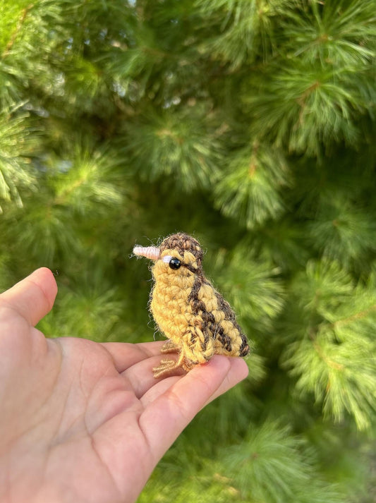 Hand holding a small crochet bird against a green foliage background