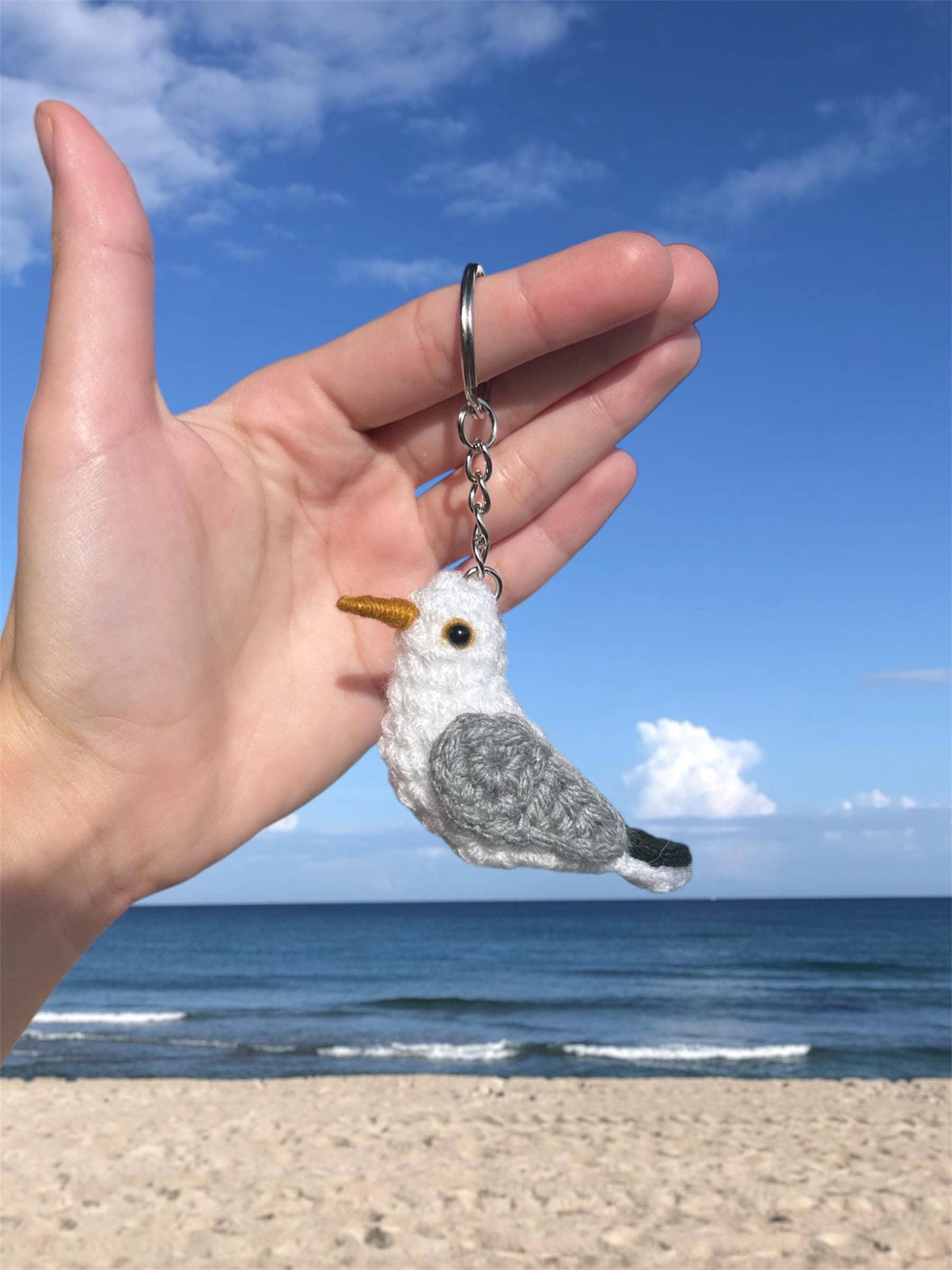 Hand holding a seagull keychain with a beach and ocean background