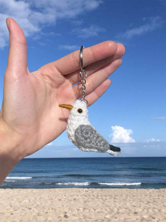 Hand holding a seagull keychain with a beach and ocean background