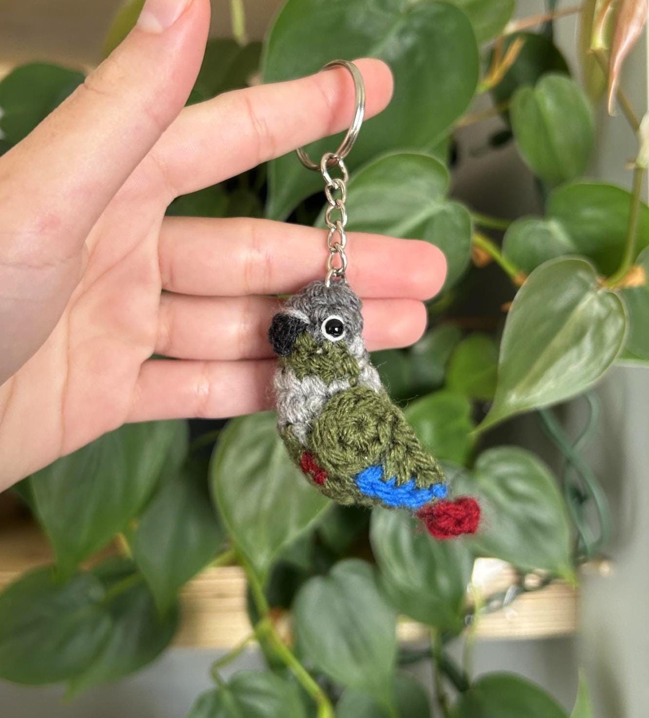 Hand holding a crocheted bird keychain with a green background