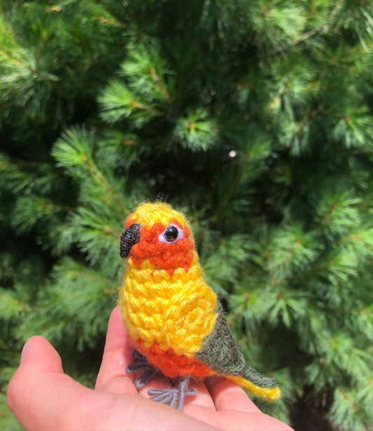 Crocheted parrot held in a hand with a green leafy background