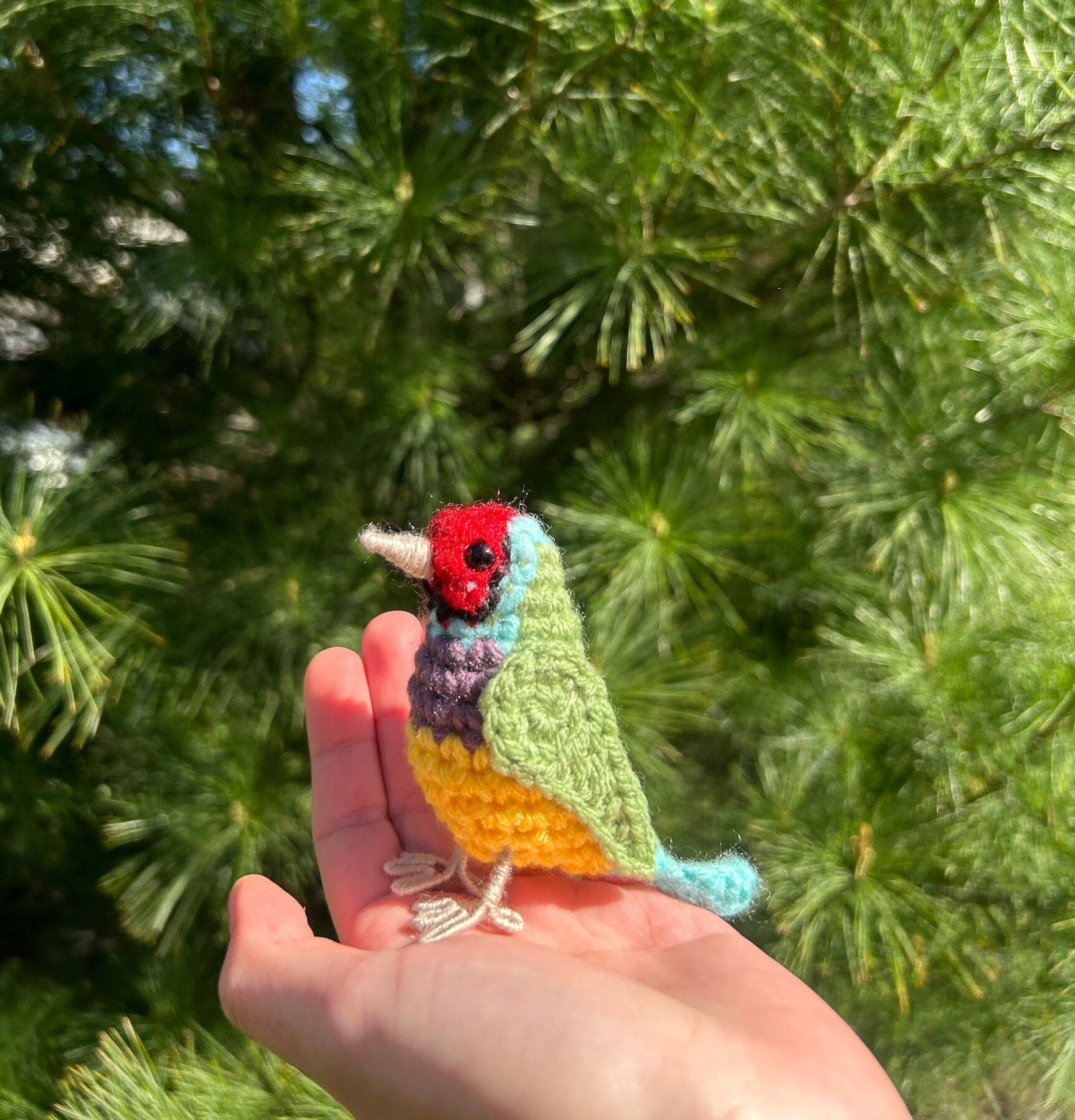 Colorful crochet bird held in a hand with a green leafy background