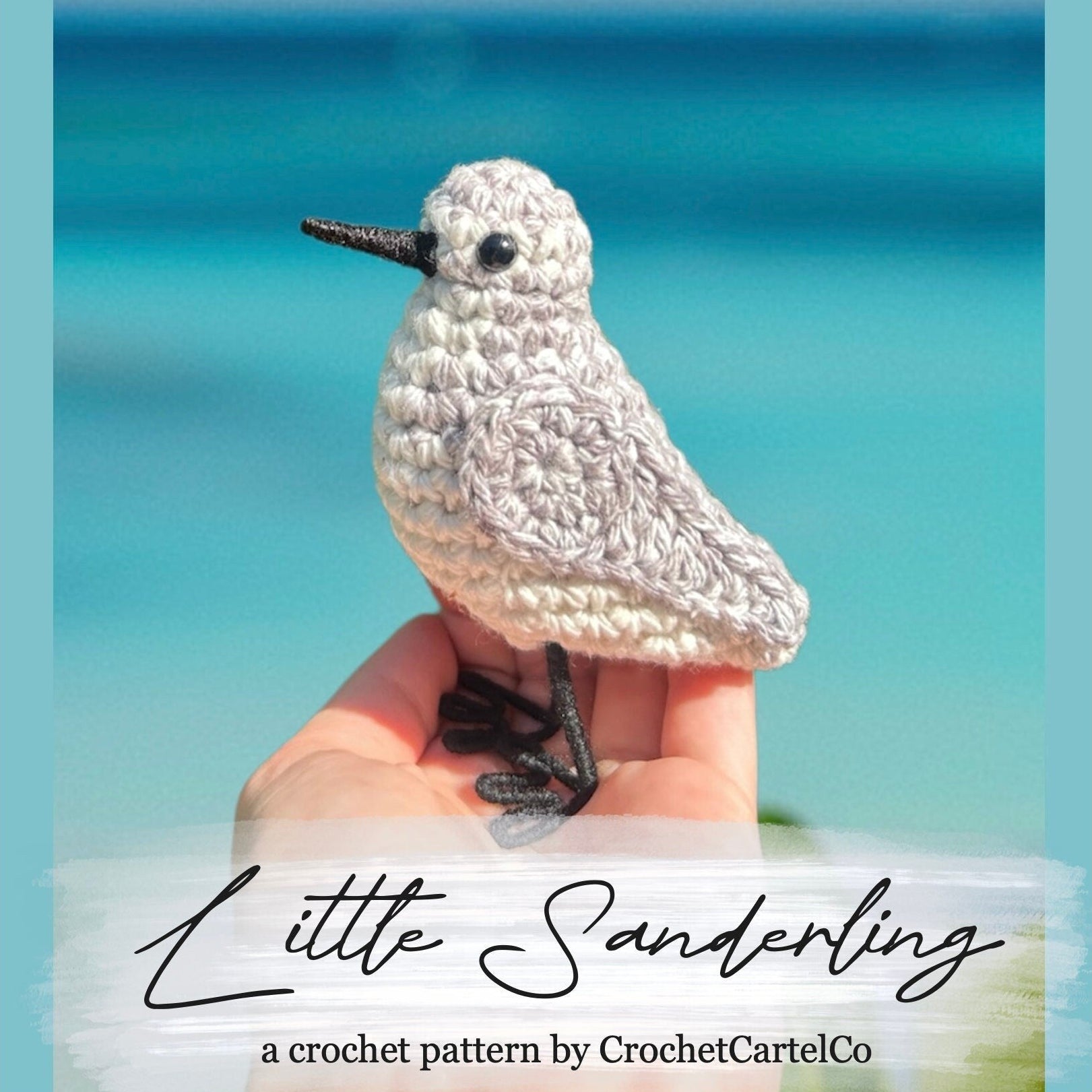 Crocheted bird held in hand with ocean background, featuring 'Little Sanderling' pattern by CrochetCartelCo.