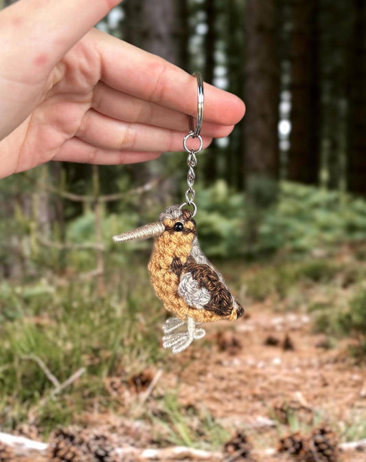 Hand holding a bird-shaped keychain with a forest background