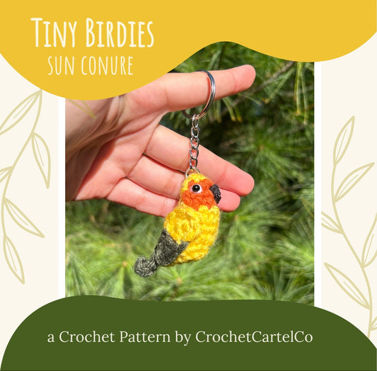 Hand holding a crochet bird keychain with 'Tiny Birdies Sun Conure, a crochet pattern by CrochetCartelCo.'