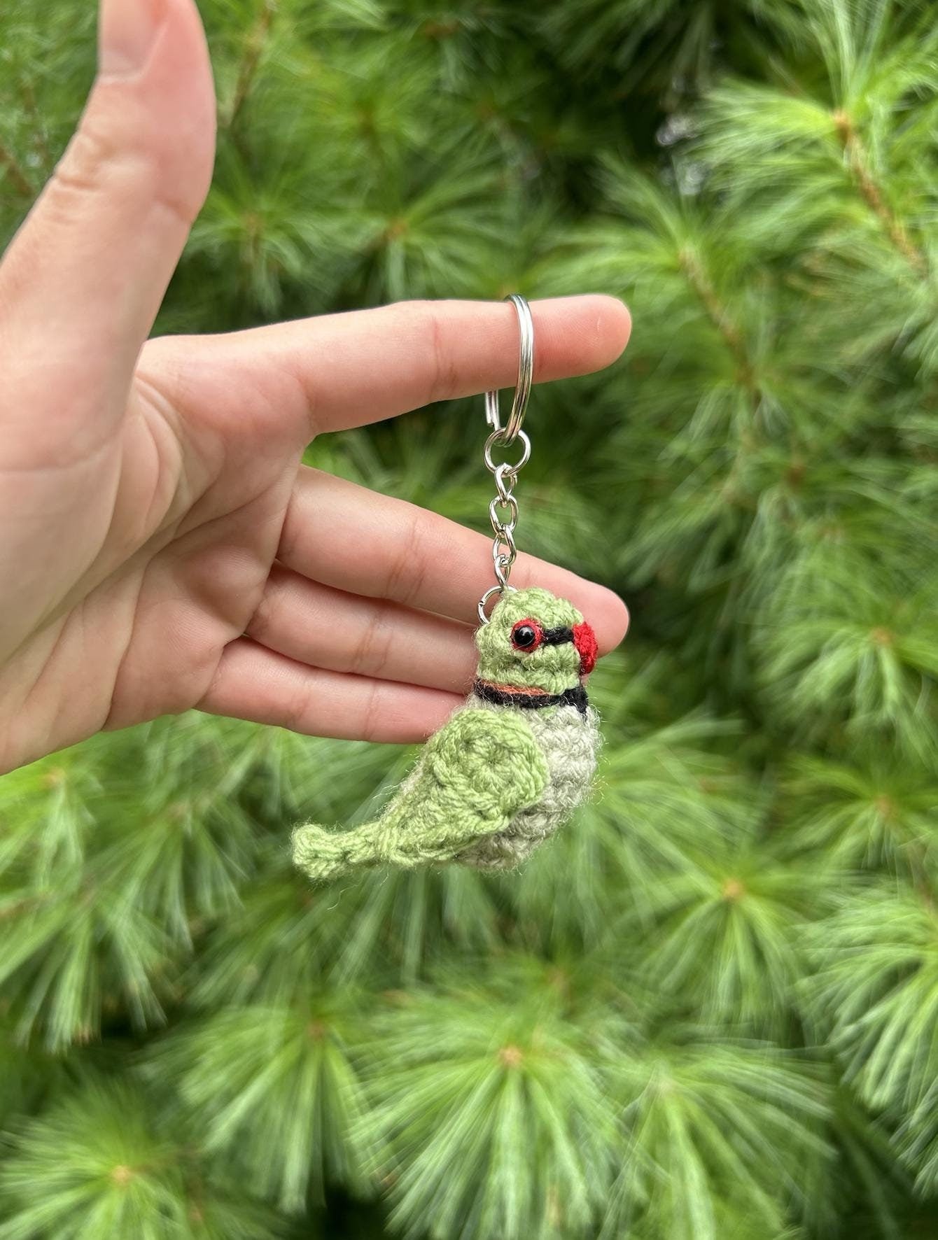 Hand holding a green bird keychain against a green foliage background