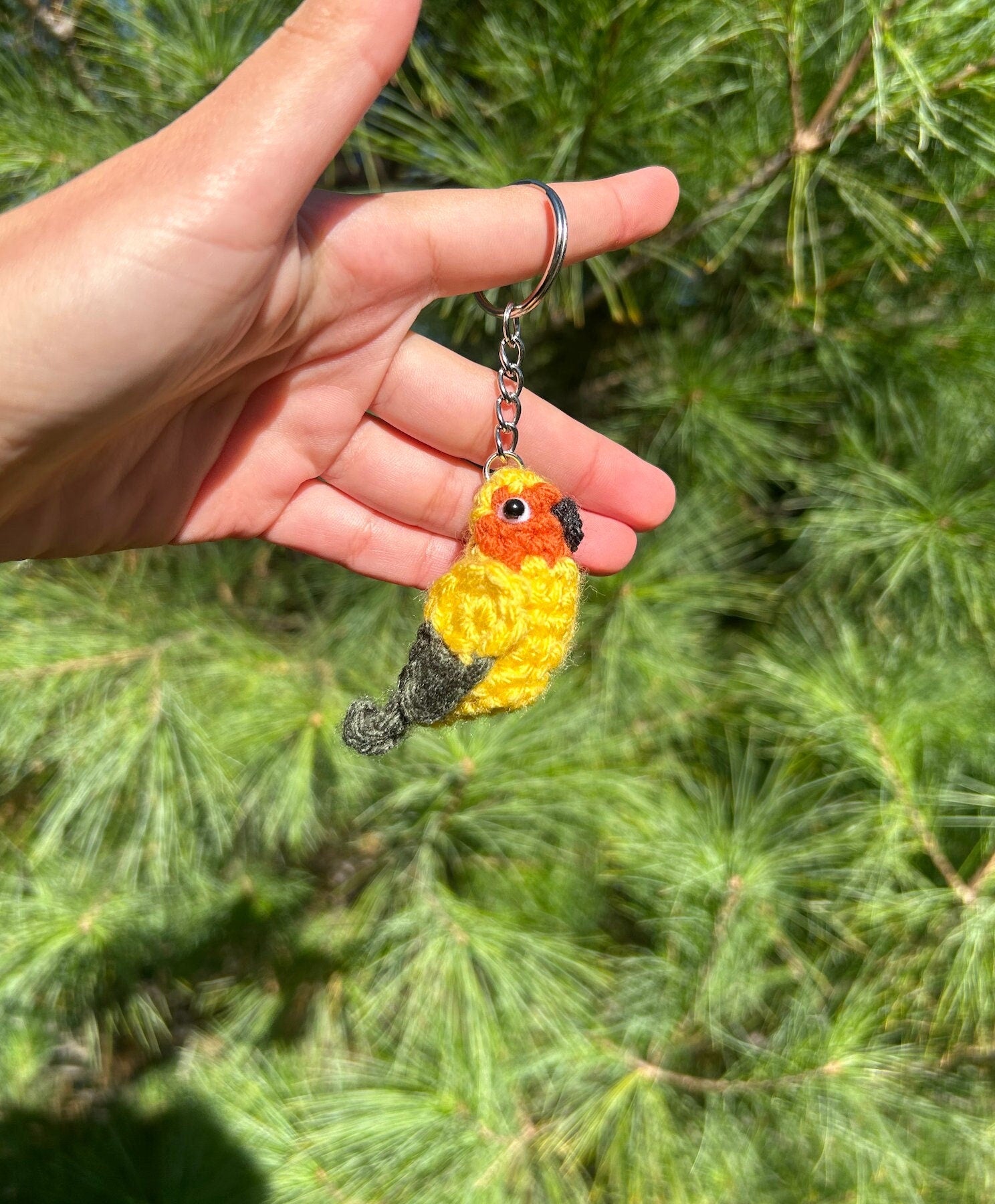 Hand holding a crocheted bird keychain with a green leafy background