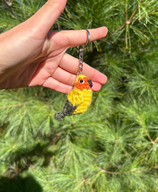 Hand holding a crocheted bird keychain with a green leafy background