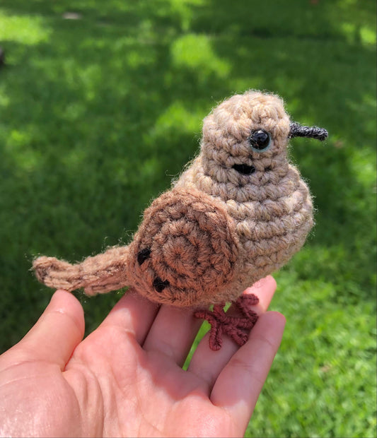 Hand holding a small crochet bird against a green outdoor background