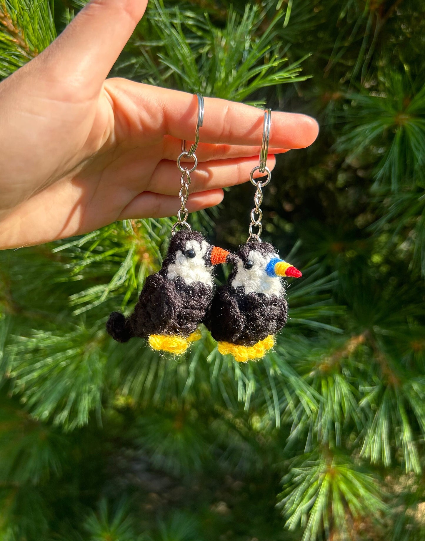 Hand holding two crochet toucan keychains against a green leafy background