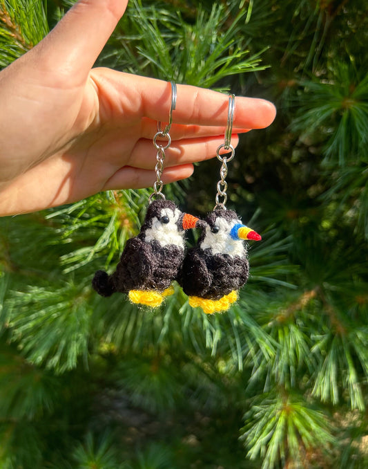 Hand holding two crochet toucan keychains against a green leafy background