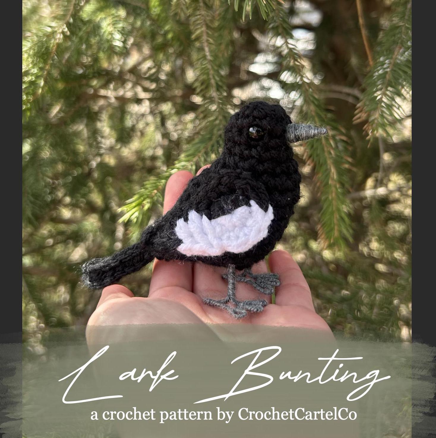 Crochet pattern for a crochet lark bunting. The bird is being held and is displayed with a blurred green background