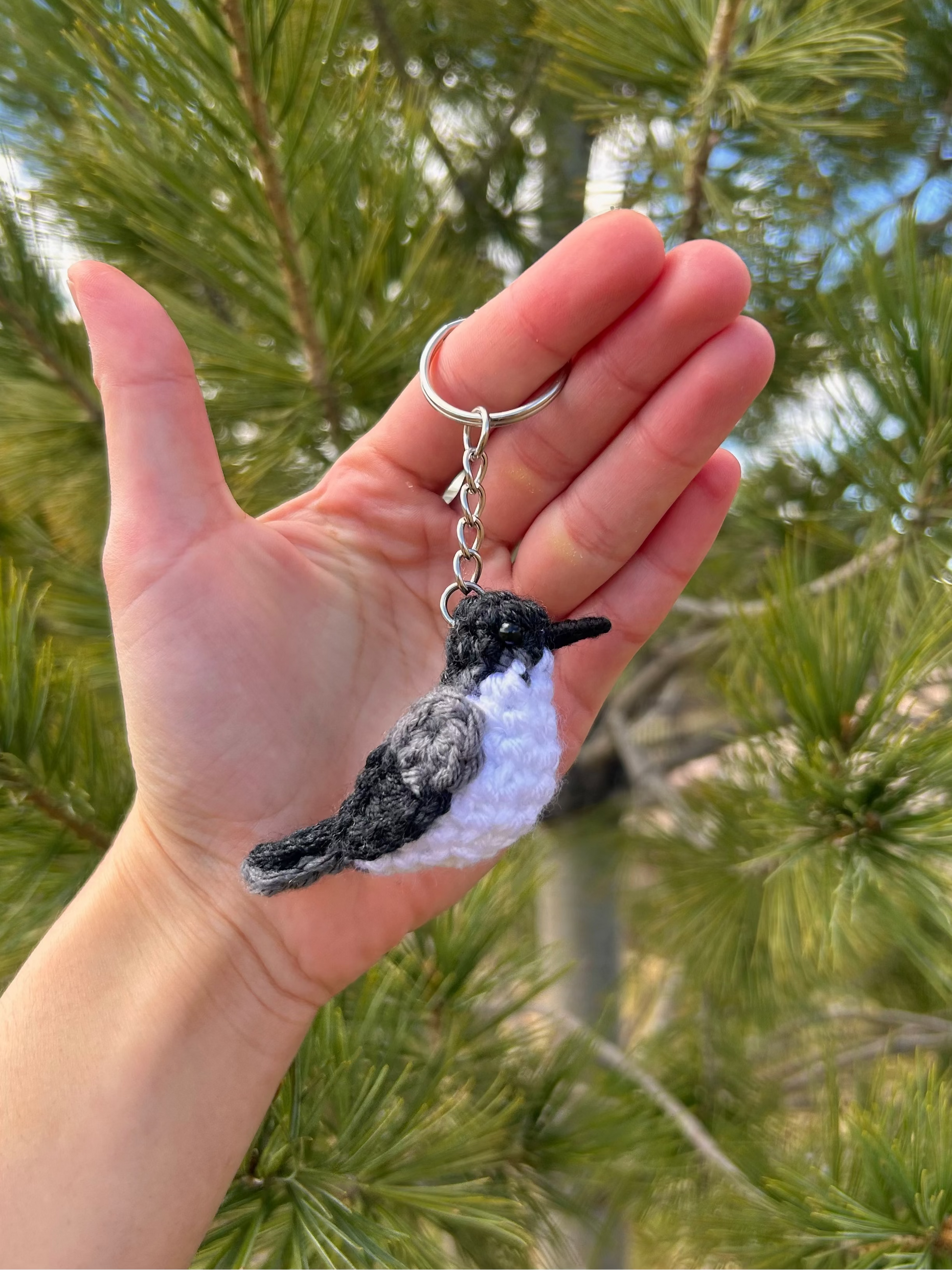 Hand holding a bird-shaped keychain with a pine tree background