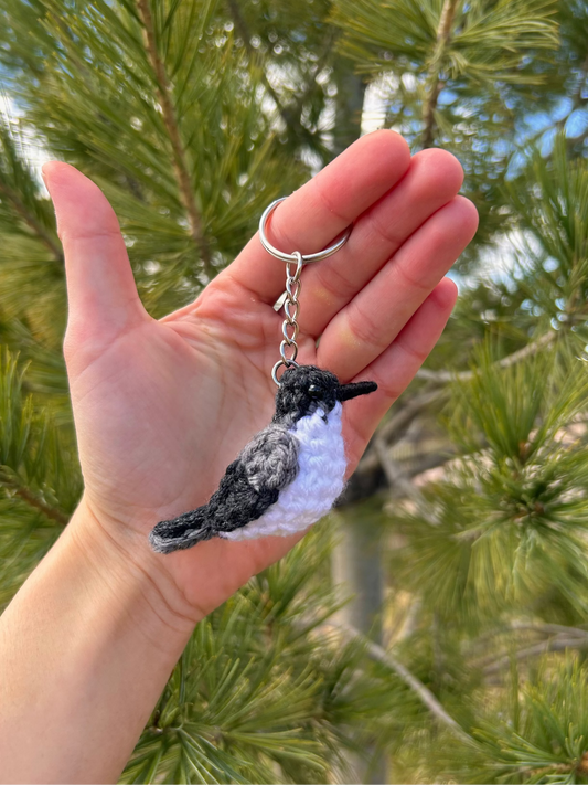 Hand holding a bird-shaped keychain with a pine tree background