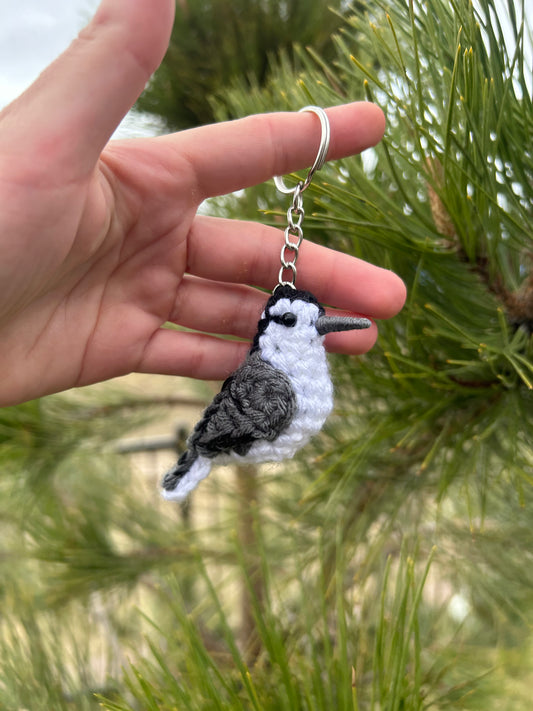 Hand holding a keychain with a bird design against a green foliage background