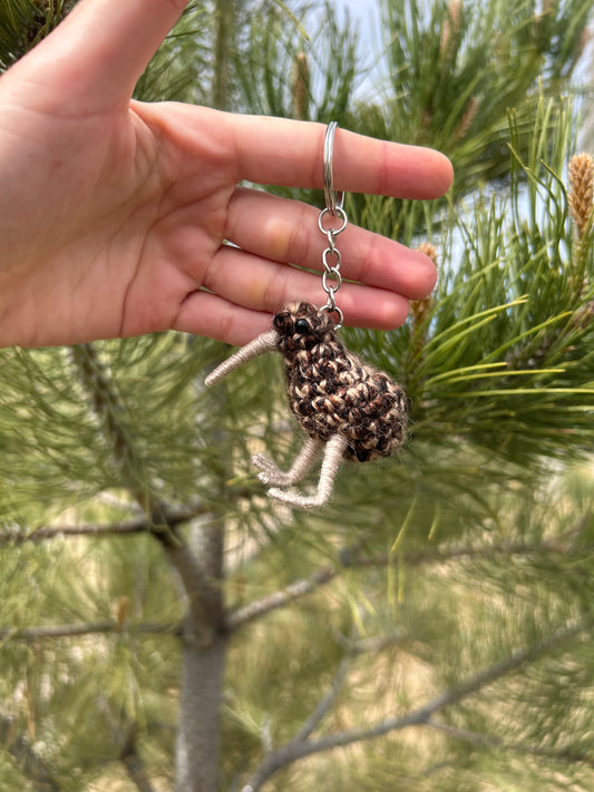 Hand holding a crochet kiwi bird keychain against a natural background