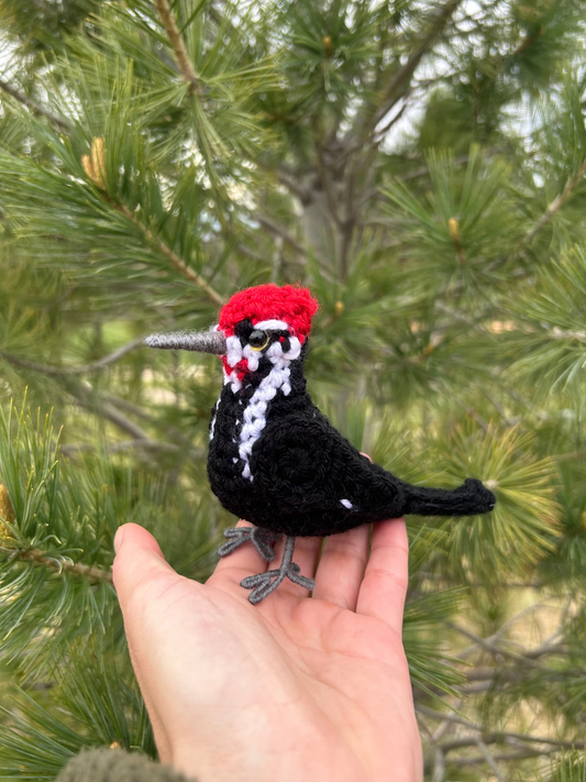 A little crochet pileated woodpecker shown with green foliage in the background
