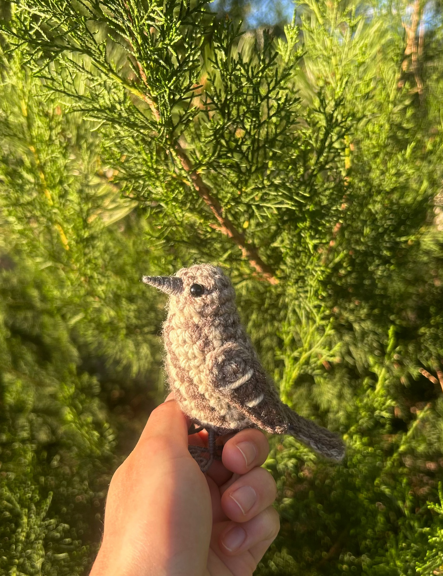 Hand holding a small bird figurine in front of green foliage