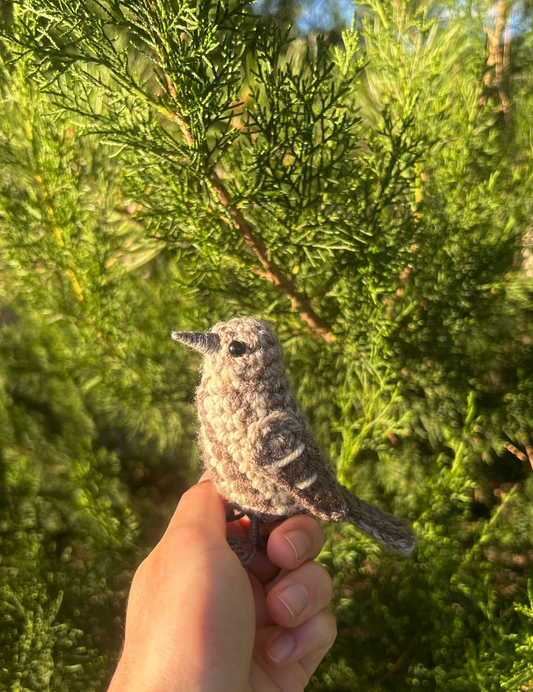 Hand holding a small bird figurine in front of green foliage