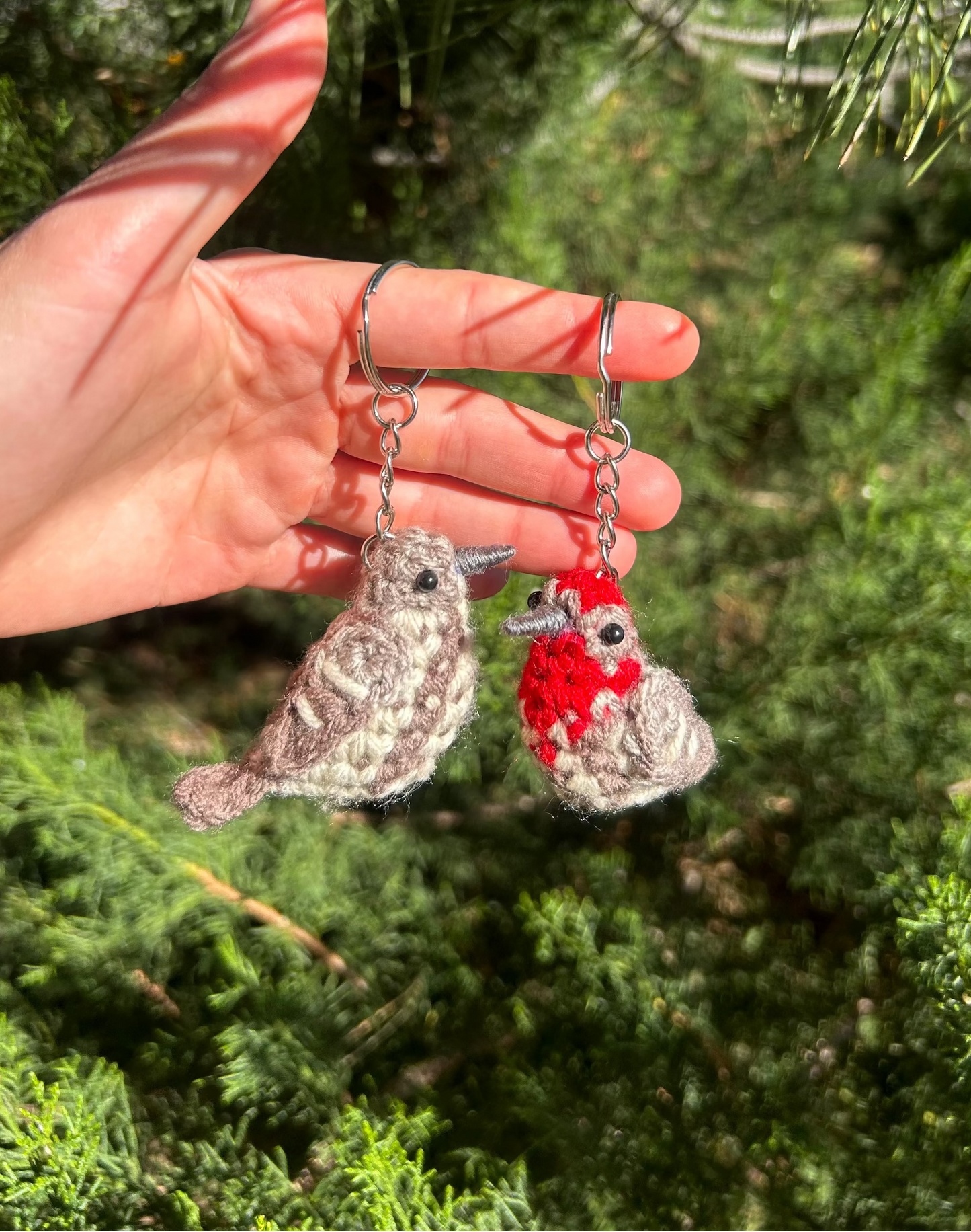 Hand holding two small bird-shaped keychains against a green tree background