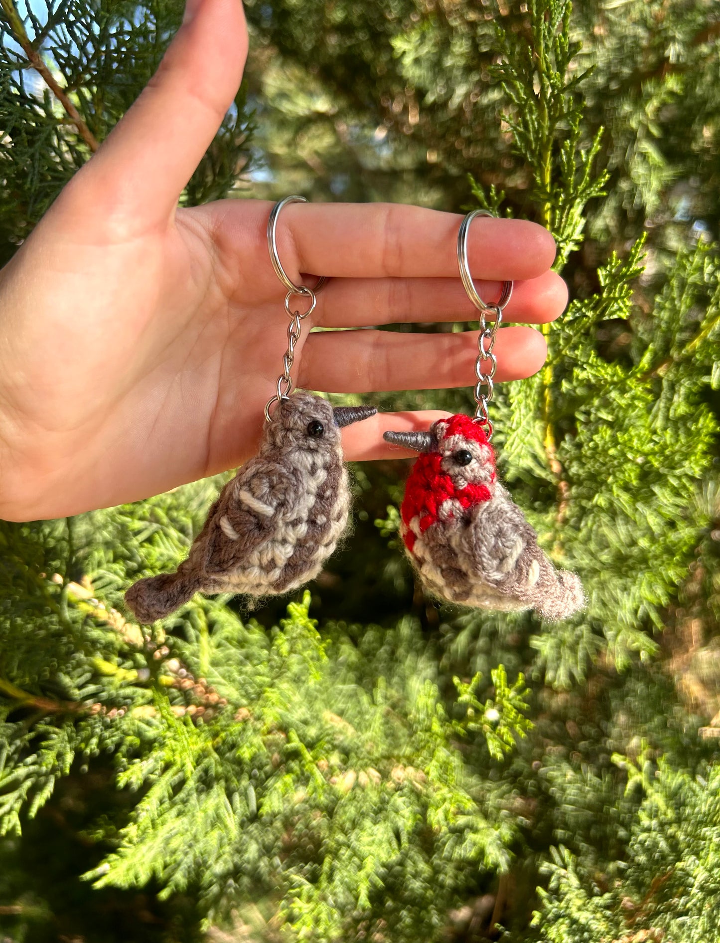 Hand holding two bird-shaped keychains against a green leafy background