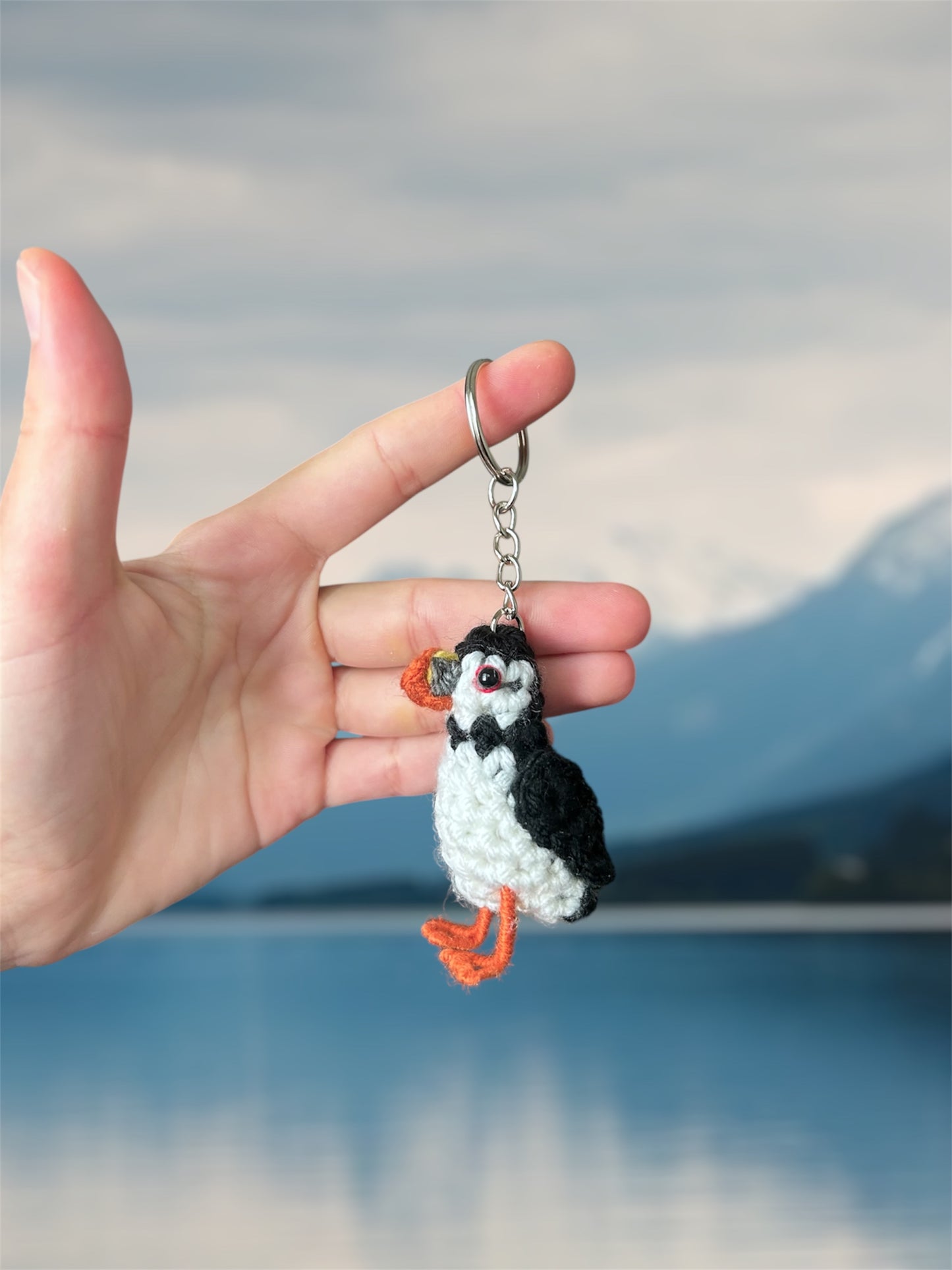 Hand holding a puffin keychain with a blurred natural background