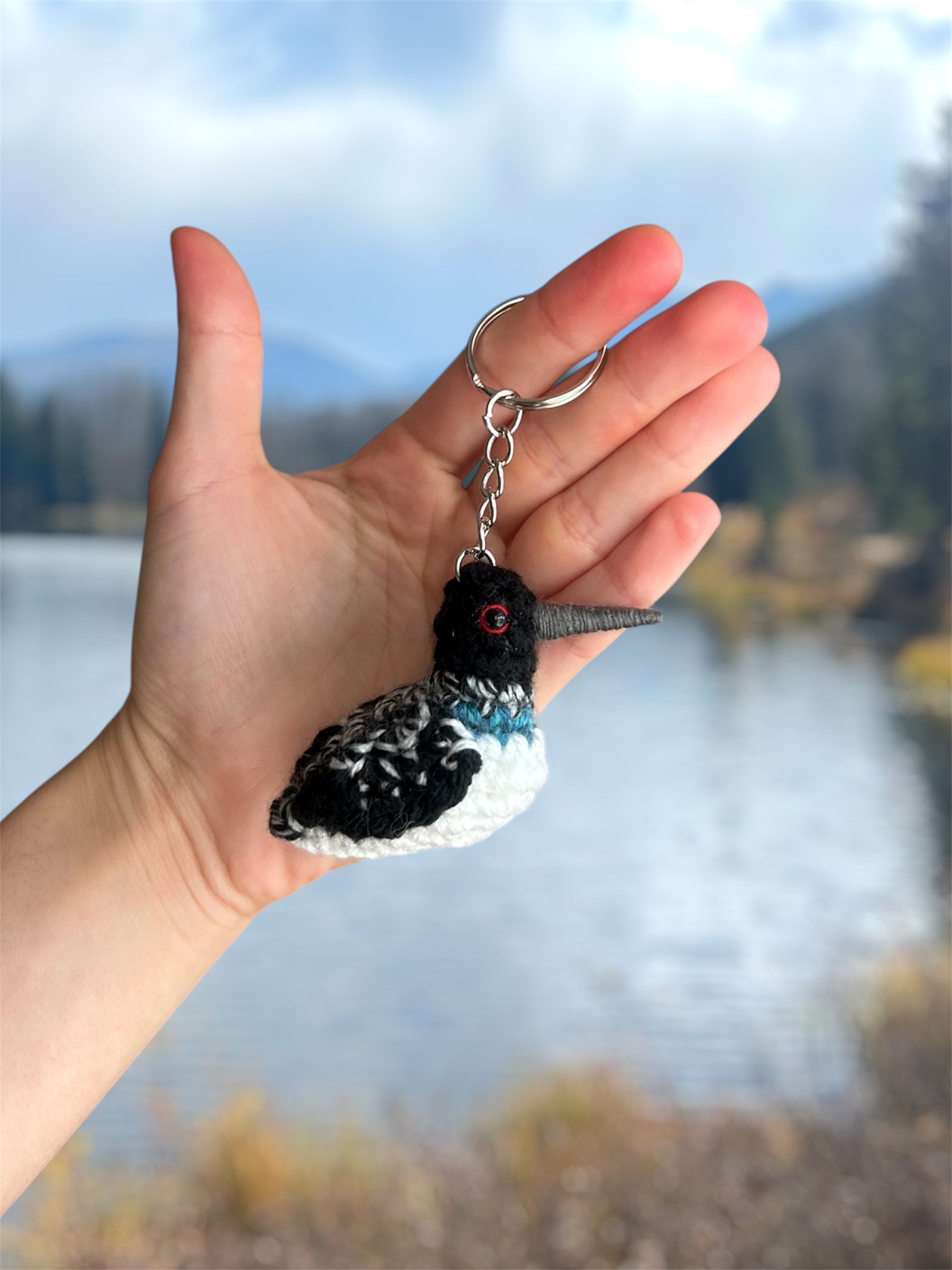Hand holding a keychain with a bird design against a blurred natural background