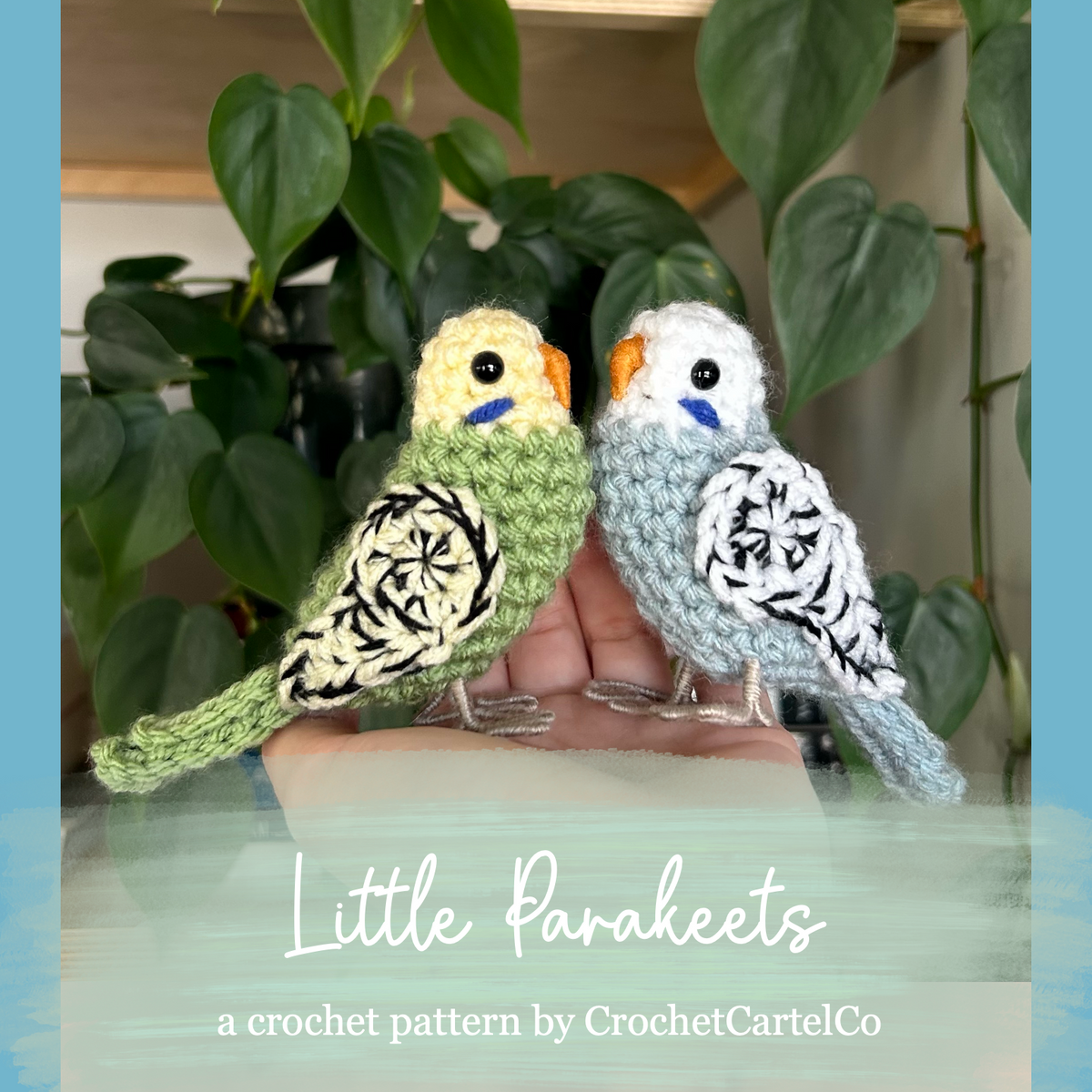 Two crocheted parakeets on a stand with green leaves in the background, featuring 'Little Parakeets Crochet Pattern' by CrochetCartelCo.