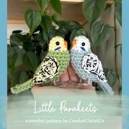 Two crocheted parakeets on a stand with green leaves in the background, featuring 'Little Parakeets Crochet Pattern' by CrochetCartelCo.