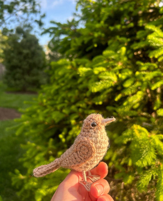 Crocheted bird held in a hand with a green outdoor background