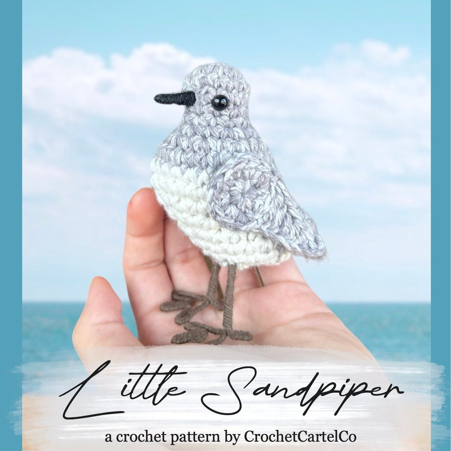 Crocheted bird held in a hand with ocean and sky background, featuring 'Little Sandpiper' pattern by CrochetCartelCo.