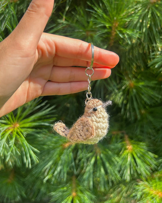 Hand holding a crochet bird keychain with a green foliage background
