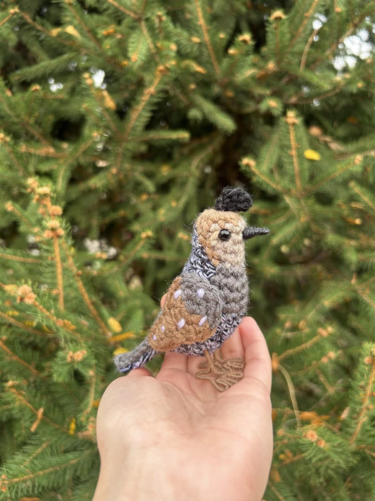 Hand holding a small bird figurine against a green tree background
