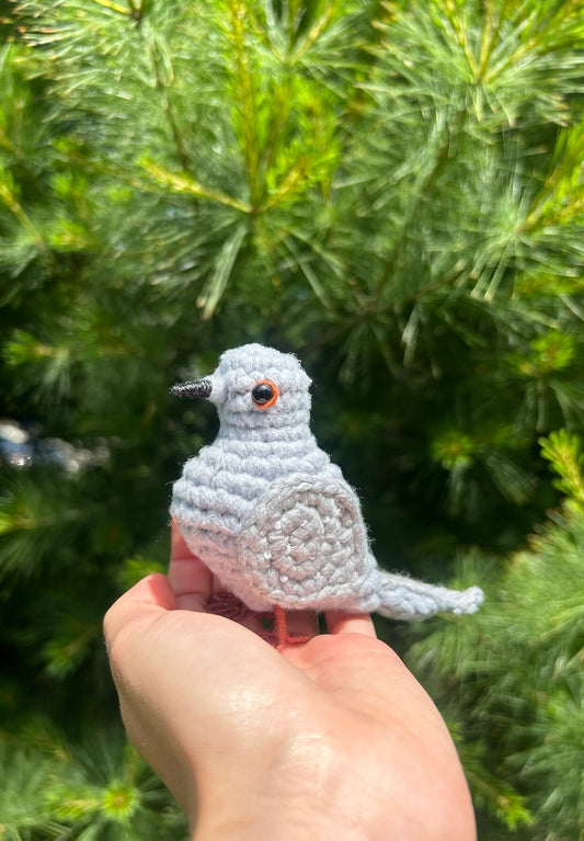 Hand holding a small crocheted bird in front of green foliage