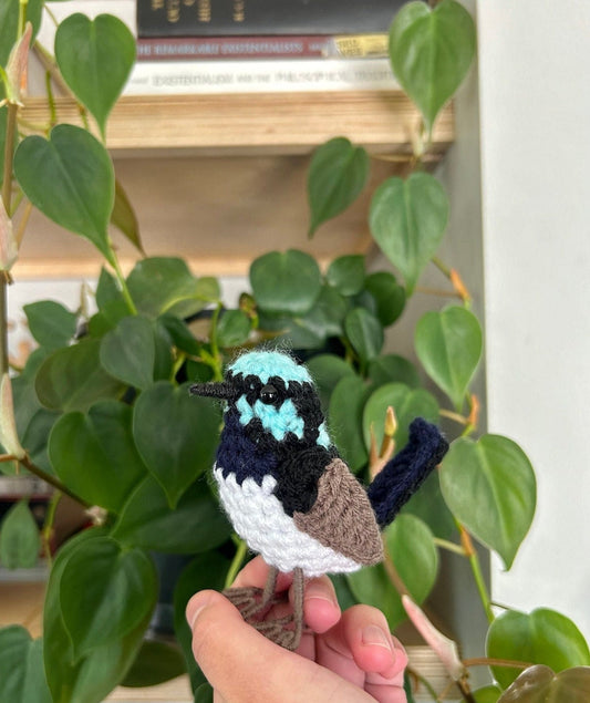 Handmade crochet bird toy held in front of green plants