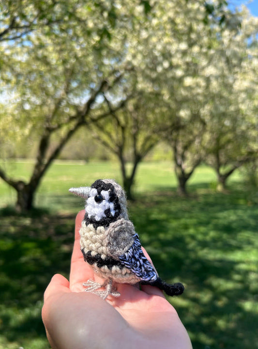 Hand holding a small bird figurine with a blurred orchard background