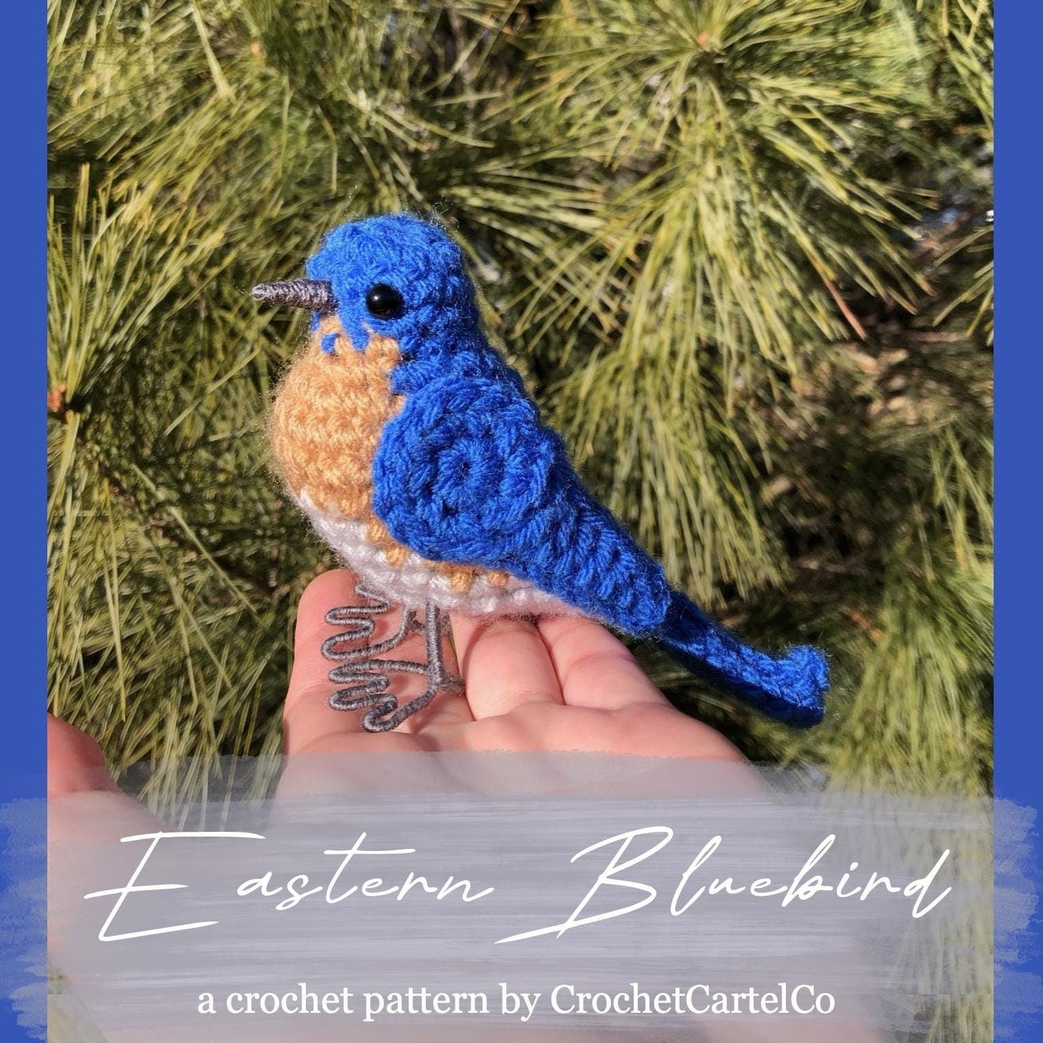 Hand holding a blue and orange crochet Eastern Bluebird in front of green foliage, with text overlay "a crochet pattern by CrochetCartelCo."